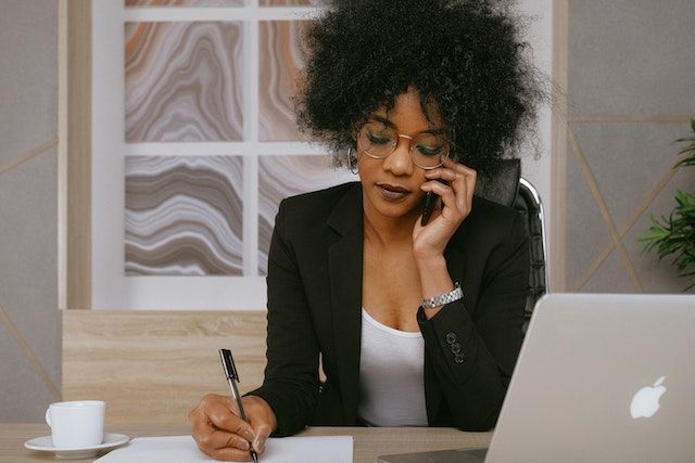 Person-sitting-at-a-desk-and-making-a-phone-call-while-taking-notes